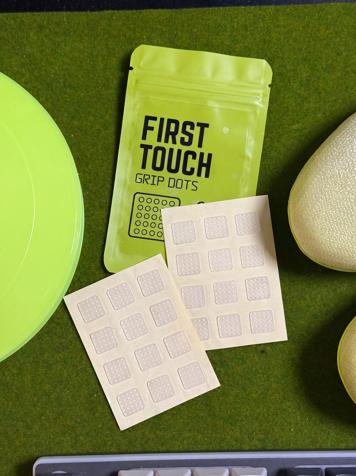 Grip Dots pouch and two patch sheets laid out on green turf beside a training cone and a cleat